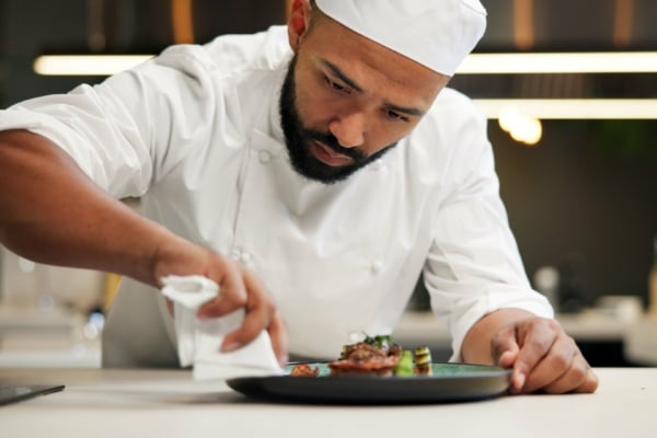 A male chef, plating up food in a restaurant kitchen
