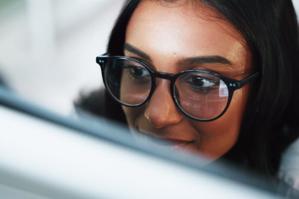 Close up image of a woman's face wearing glasses. In the reflection of glasses a computer screen can be seen.