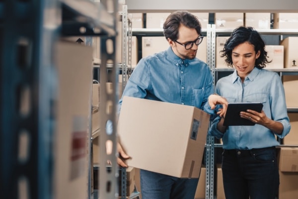 Female Inventory Manager Shows Digital Tablet Information to a Worker Holding Cardboard Box.