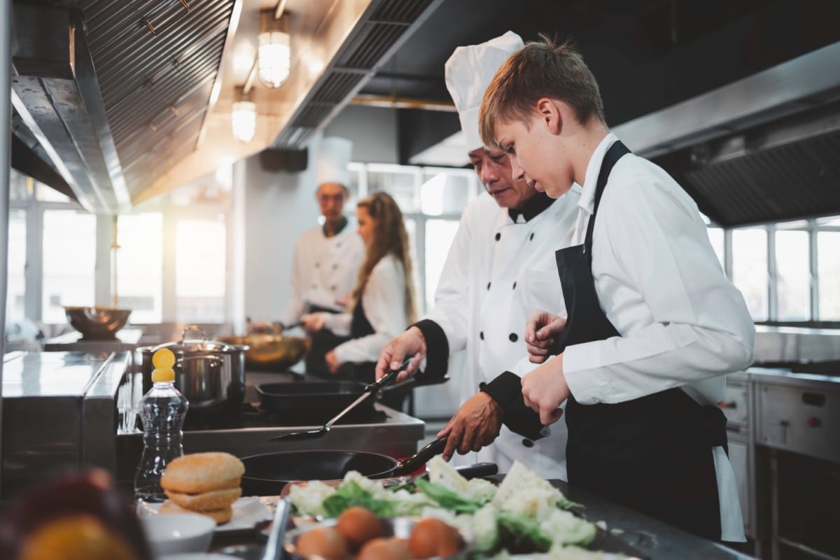 Trainee chef learning from a qualified chef in a professional kitchen setting