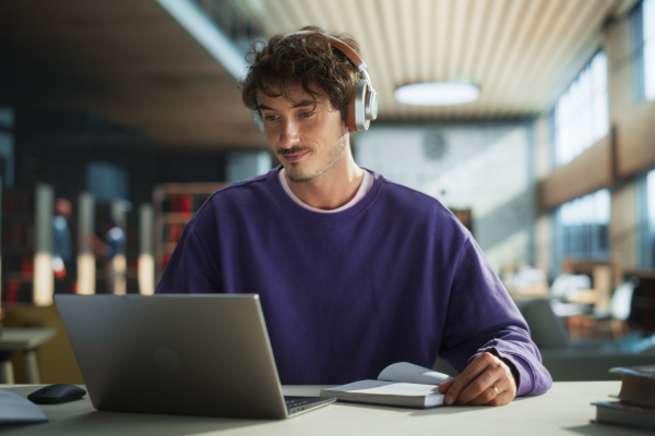 A young man working on a laptop and wearing headphones