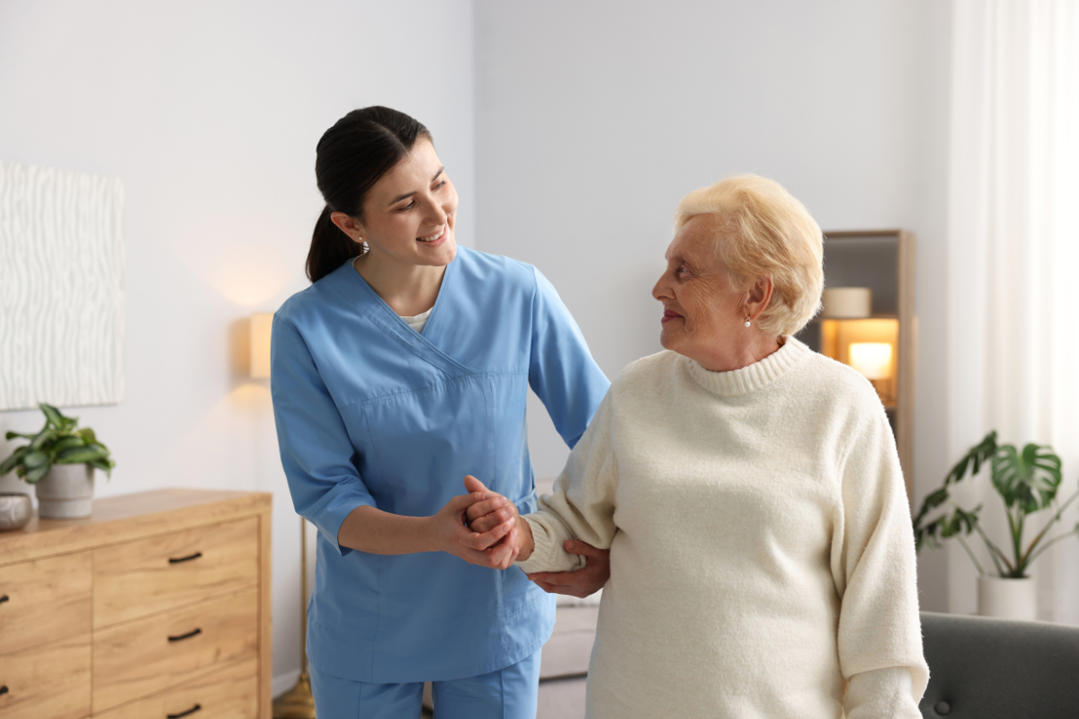 A care worker helping an elderly woman walk across a room