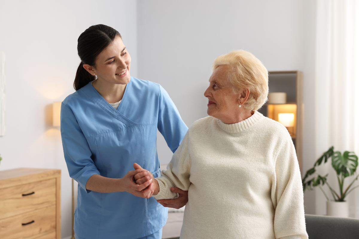 Care working helping an elderly patient to move around a room