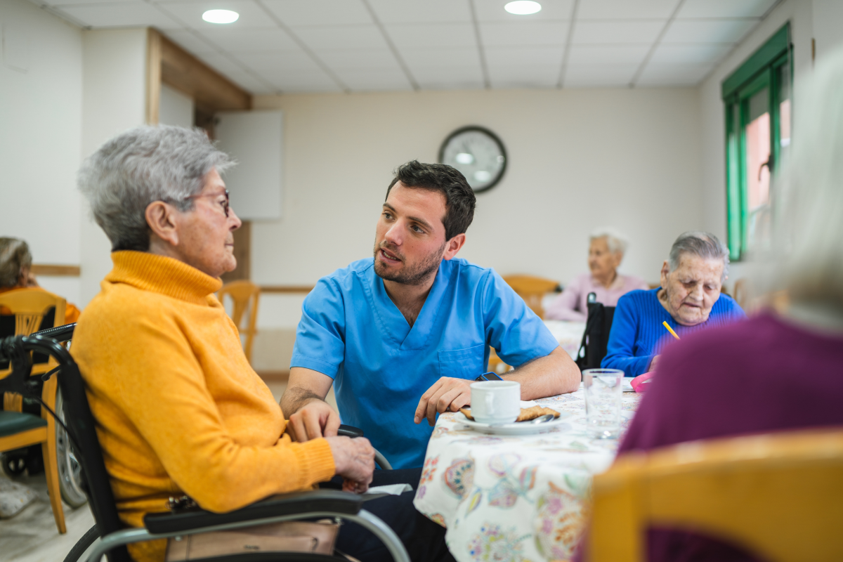 male care worker providing assistance and talking with an elderly woman in a wheelchair during an activity at a care home