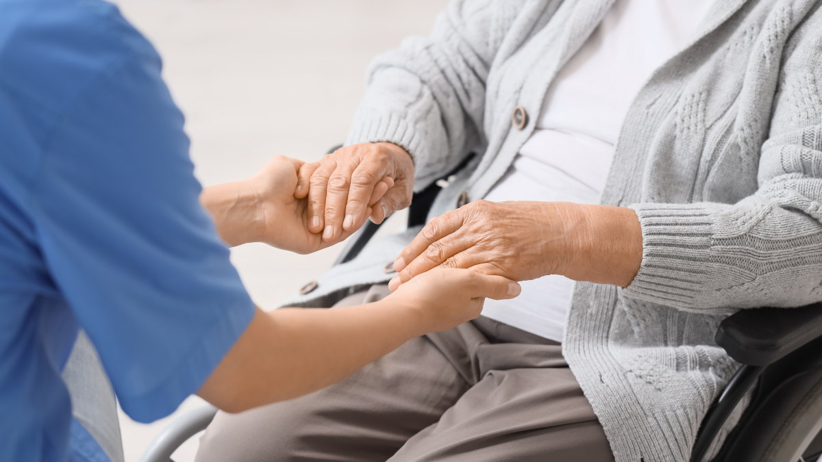 Nurse with senior woman in wheelchair holding hands