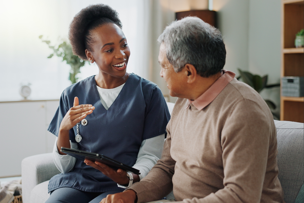 Woman care worker talking to elderly male person with technology for advice
